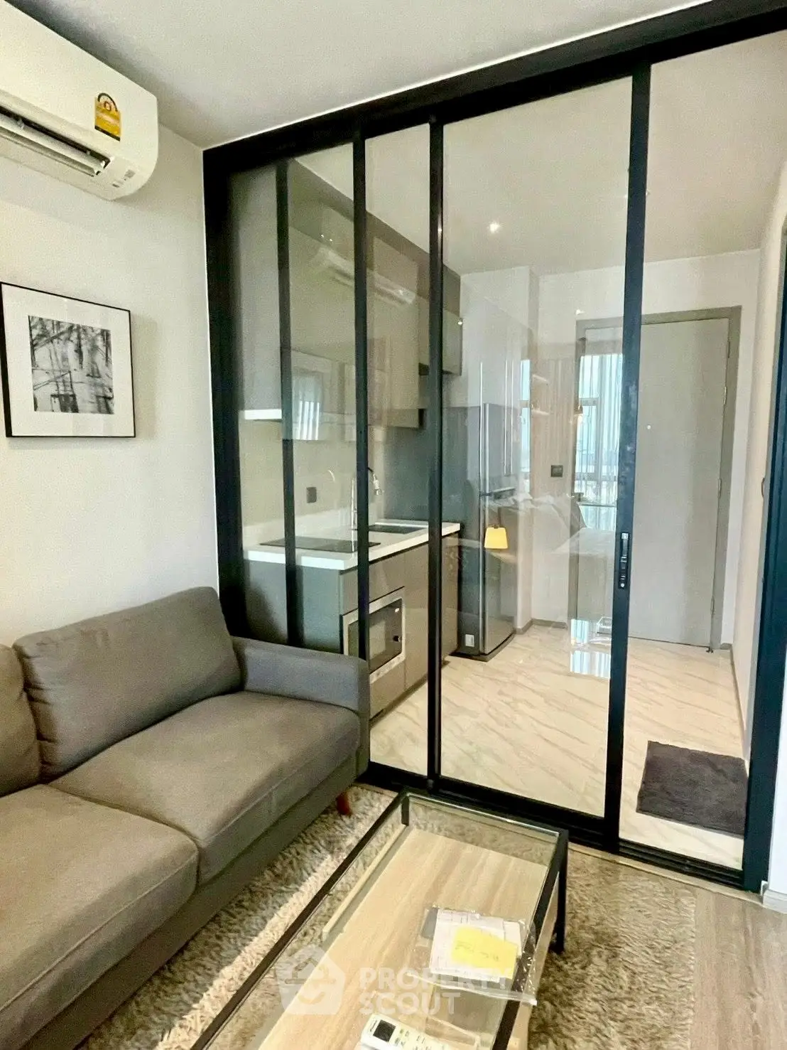 Modern living room with glass partition and compact kitchen in stylish apartment.