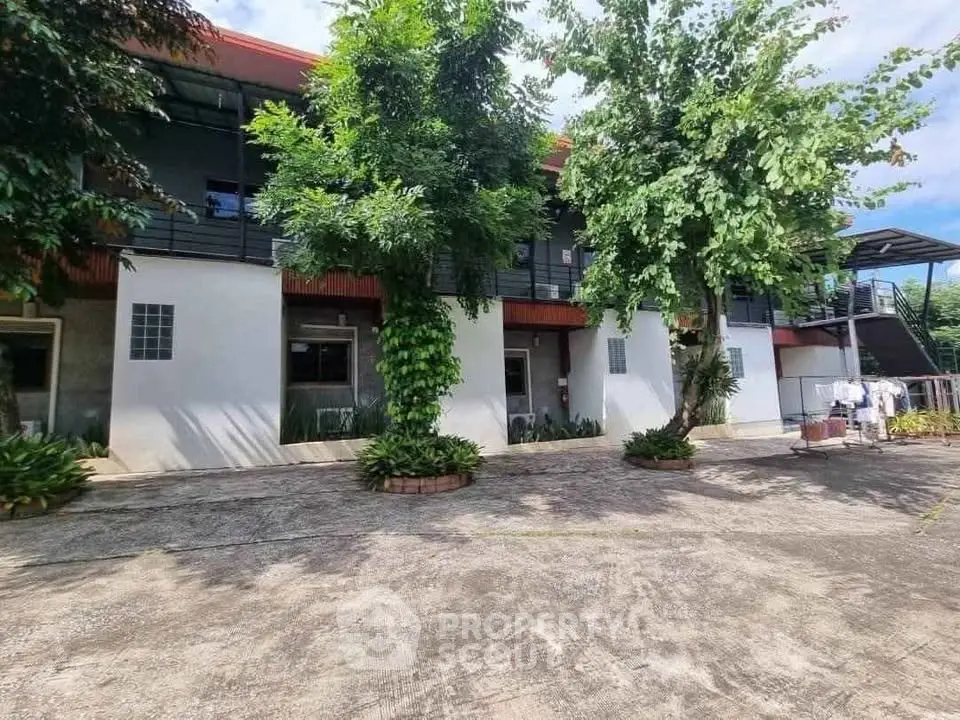 Modern building exterior with lush greenery and spacious courtyard.