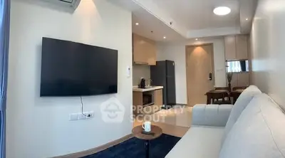Modern living room with open kitchen, featuring sleek furniture and wall-mounted TV.