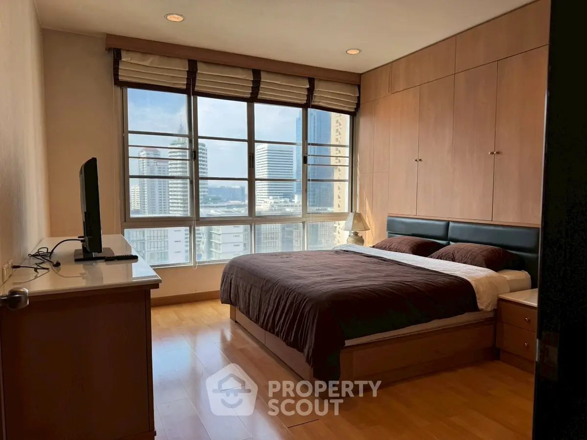 Spacious bedroom with city view and modern furnishings in high-rise apartment.