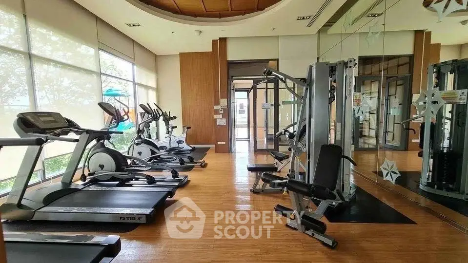 Spacious gym with modern fitness equipment and large windows for natural light.
