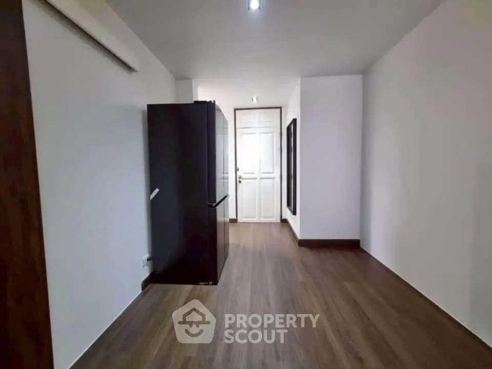 Spacious room with sleek wooden flooring and modern black refrigerator, ideal for versatile use.