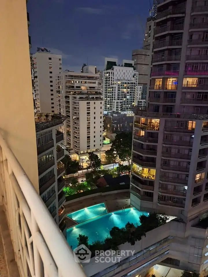 Stunning cityscape view from balcony overlooking illuminated pool and modern high-rise buildings.