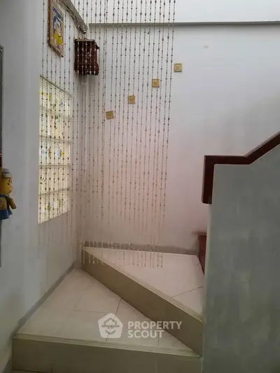 Charming staircase with decorative beaded curtain and natural light in cozy home interior.