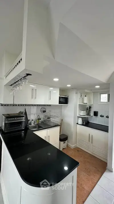Modern kitchen with sleek black countertops and white cabinetry, featuring built-in appliances and stylish lighting.