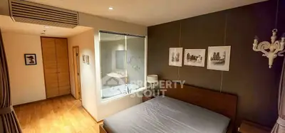Modern bedroom with glass wall view into bathroom, wooden flooring, and stylish decor.
