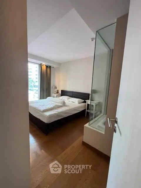 Spacious bedroom with wooden flooring and large window for natural light.