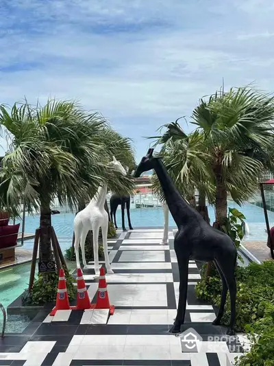 Luxurious poolside area with artistic giraffe sculptures and palm trees, offering a serene waterfront view.