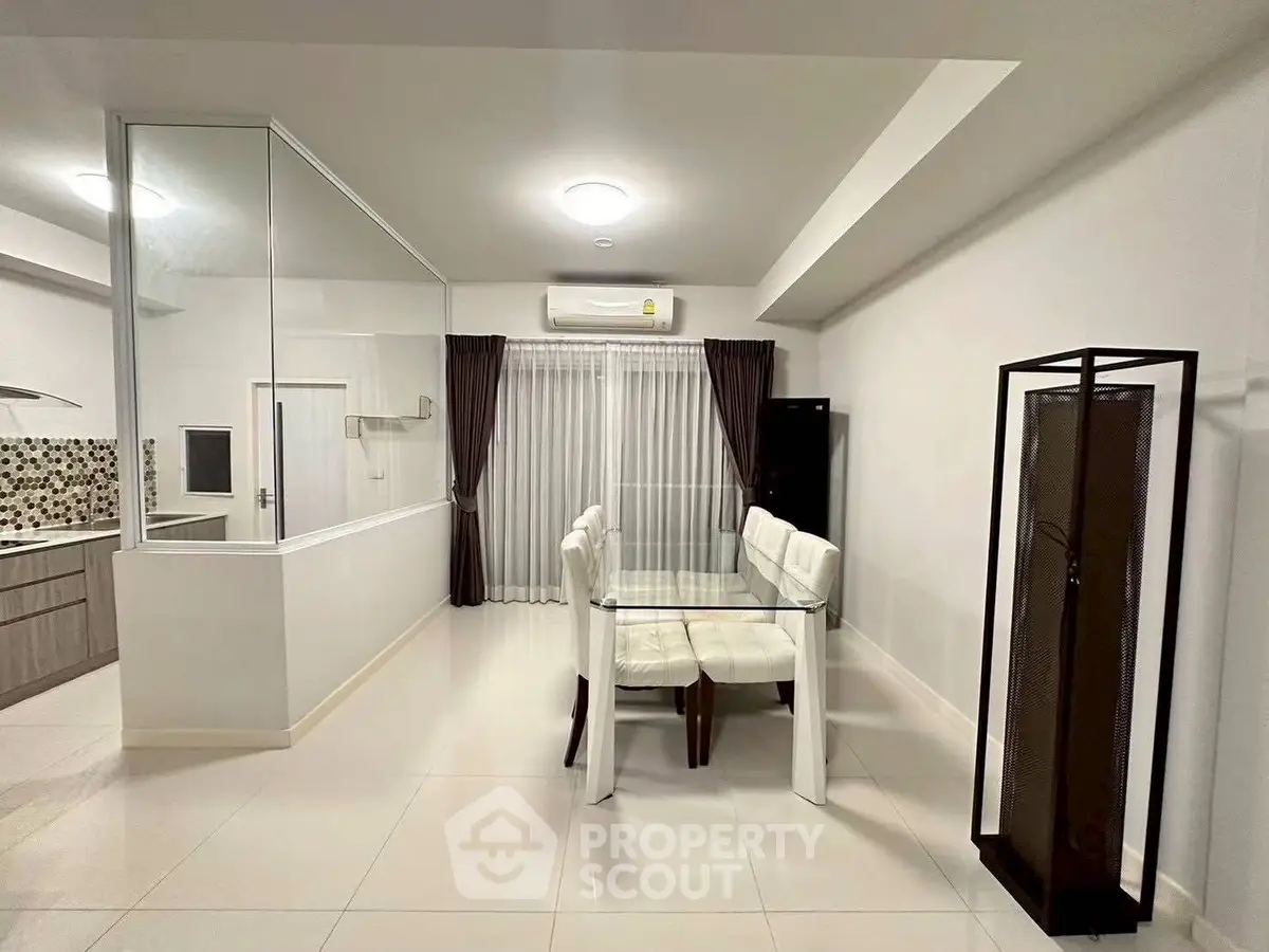 Modern dining area with glass table and white chairs in open layout apartment.