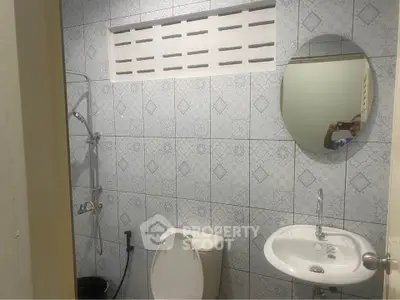 Compact bathroom with tiled walls, round mirror, and basic fixtures.