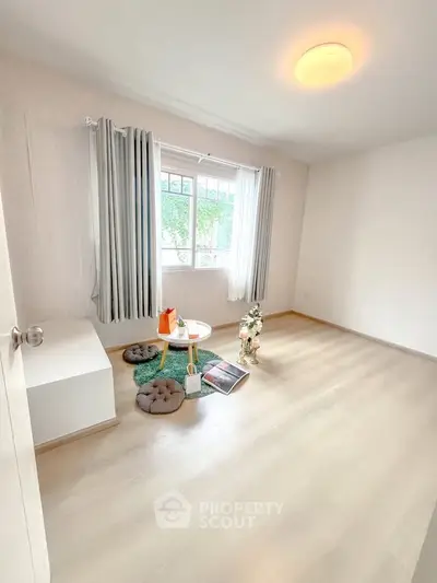 Bright minimalist room with large window and light wood flooring, perfect for cozy living.