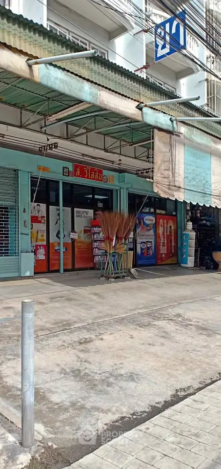 Street view of a local shop with colorful signage and broom display in front, showcasing urban retail space.