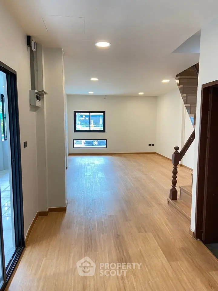 Spacious open-plan living room with wooden flooring and staircase, ideal for modern living.