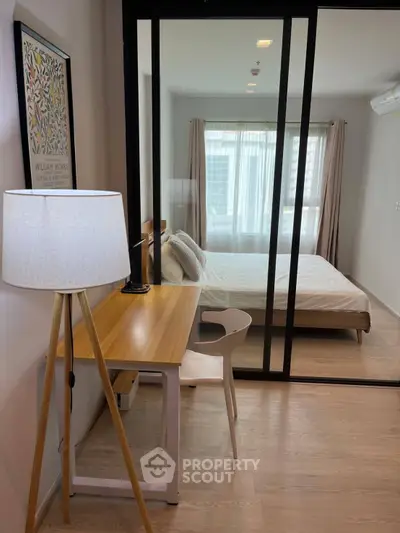 Modern bedroom with glass partition and cozy study area, featuring natural light and stylish decor.