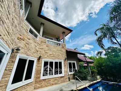 Stunning stone facade house with pool and lush greenery under a bright blue sky.