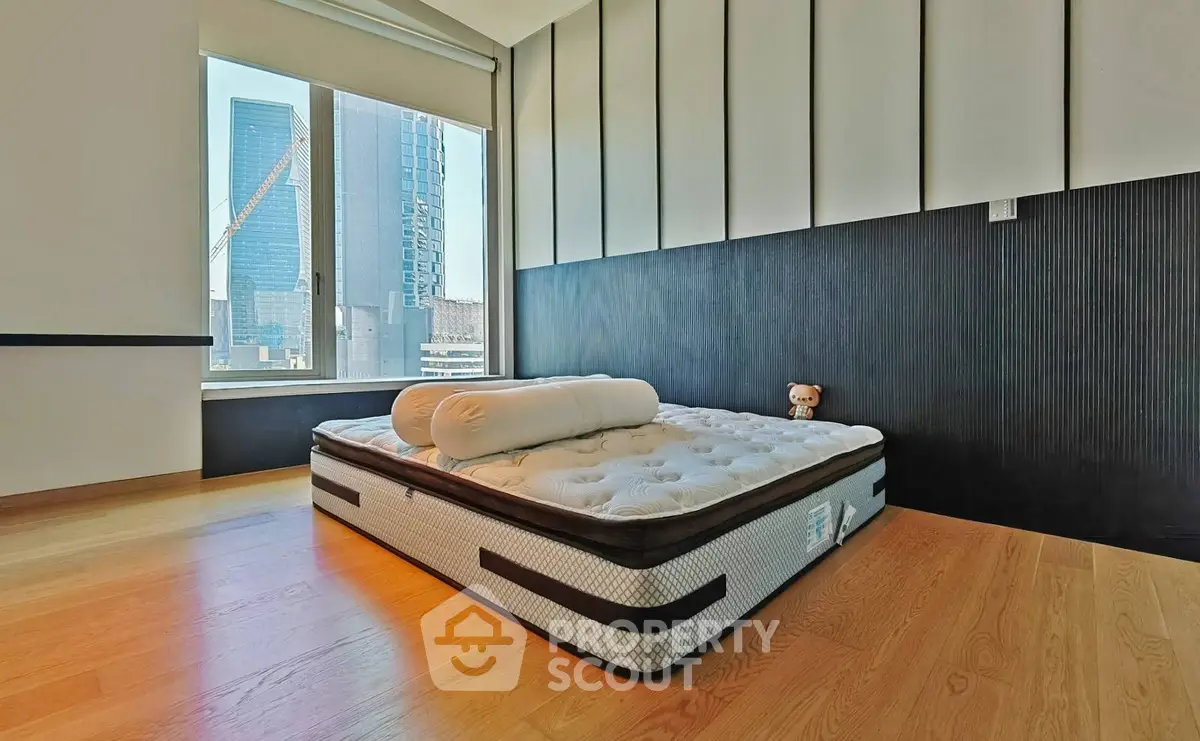 Modern bedroom with large window and city view, featuring a minimalist design and comfortable mattress.