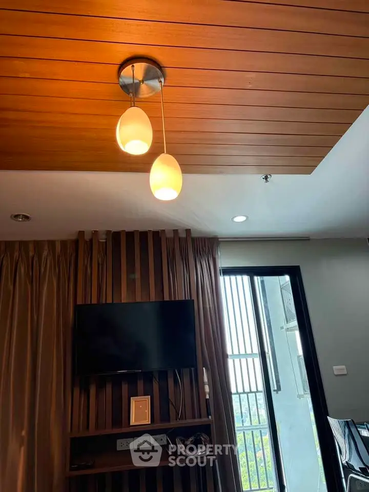 Modern living room with stylish lighting and TV setup, featuring a partial view of a balcony.