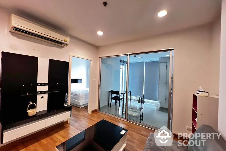 Modern living room with wooden flooring and sliding glass doors leading to a bedroom.