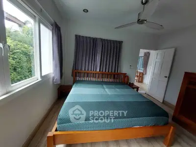 Spacious bedroom with large window and wooden bed frame, offering serene garden views.