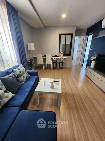 Modern living room with blue sofa and wooden flooring, featuring a cozy dining area.