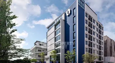Modern blue and white apartment building with lush greenery and clear sky.
