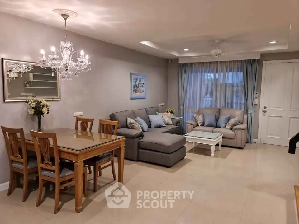 Elegant living room with chandelier, cozy seating, and dining area in modern apartment.
