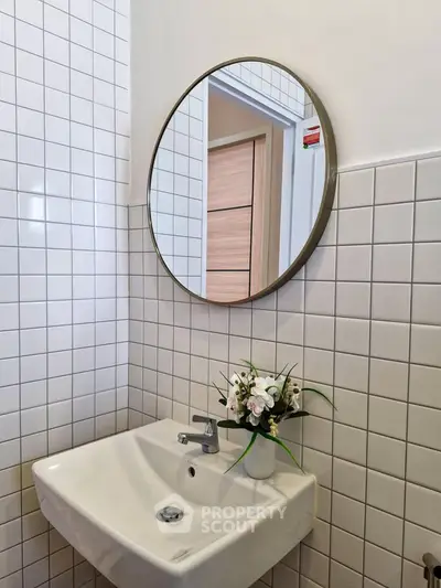 Modern bathroom with round mirror and white tiled walls, featuring a sleek sink and floral decor.