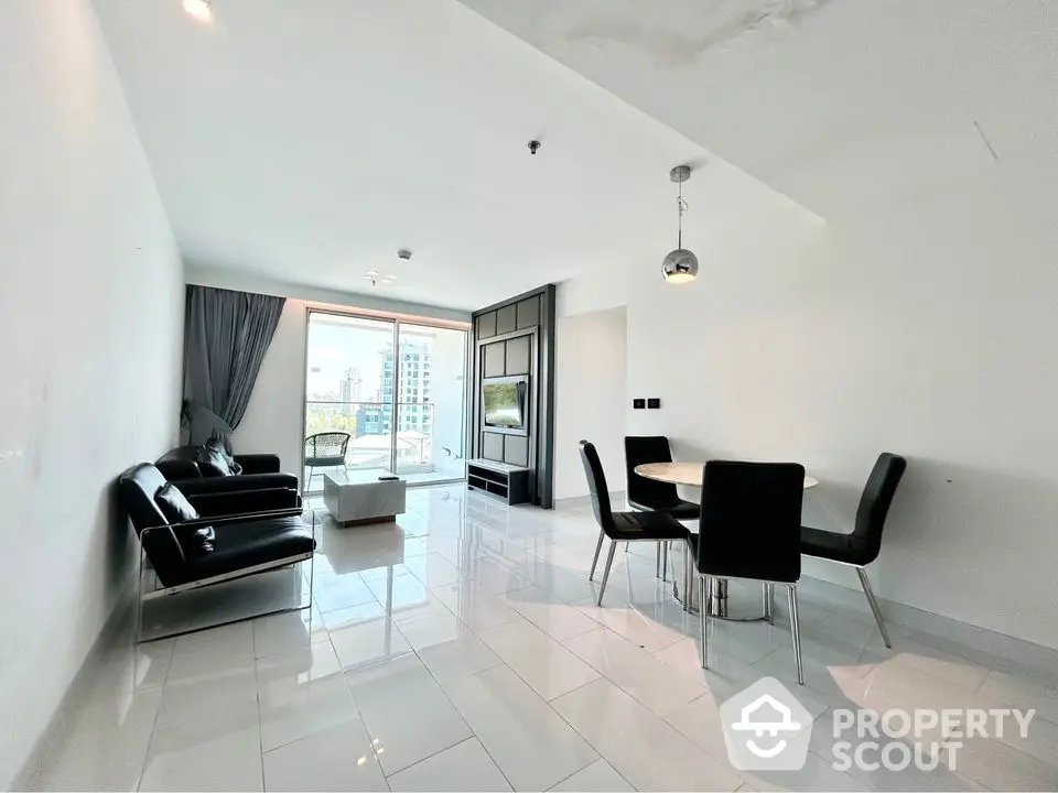 Spacious modern living room with sleek black furniture and large windows offering city views.