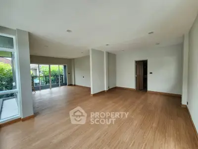 Spacious empty living room with wooden flooring and large windows leading to balcony.