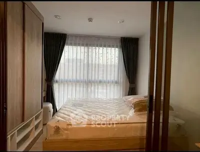 Cozy bedroom with large window and elegant curtains, featuring a comfortable bed and wooden wardrobe.