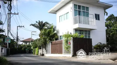 Modern two-story corner house with a spacious balcony, surrounded by lush greenery in a serene neighborhood, perfect for families seeking comfort and privacy.