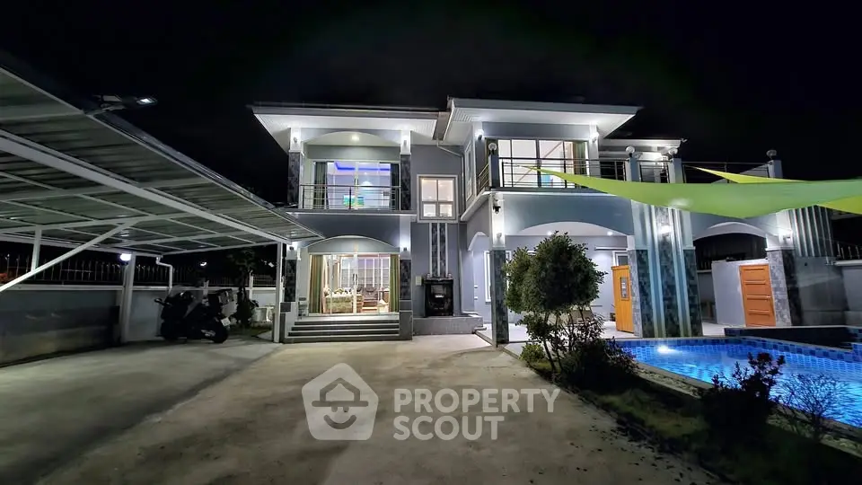 Stunning modern two-story house with pool and carport, beautifully lit at night, showcasing luxury living.