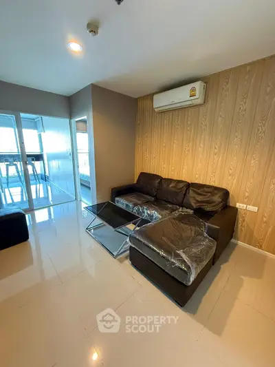 Modern living room with sleek black sofa and glass coffee table, featuring large windows and air conditioning.