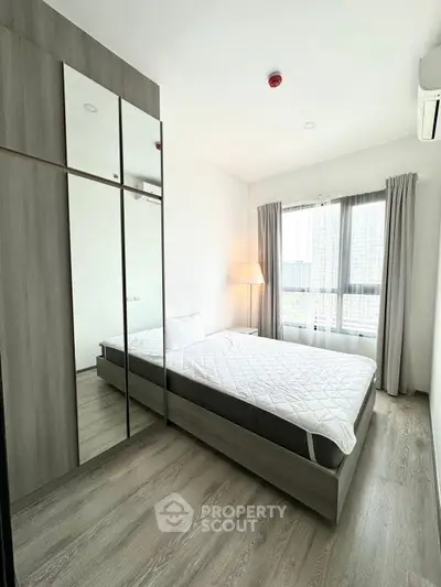 Modern bedroom with large window and mirrored wardrobe in high-rise apartment.