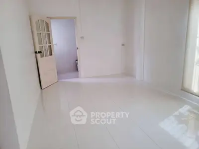 Spacious empty room with white tiled floor and open door, ready for customization.