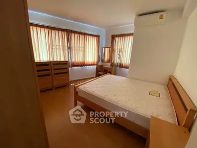 Cozy bedroom with wooden furniture and natural light, featuring an air conditioner for comfort.