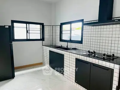 Modern kitchen with sleek black cabinetry and gas stove, featuring stylish tiled backsplash and large windows.