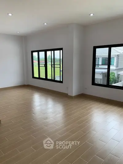 Spacious empty room with large windows and wooden flooring, perfect for customization.