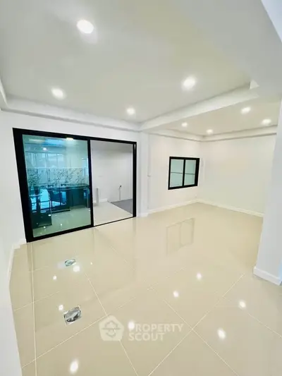 Spacious modern living room with sleek tile flooring and recessed lighting, featuring a glass sliding door.