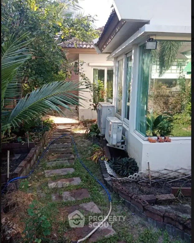 Charming garden pathway leading to a cozy home with lush greenery and modern windows.