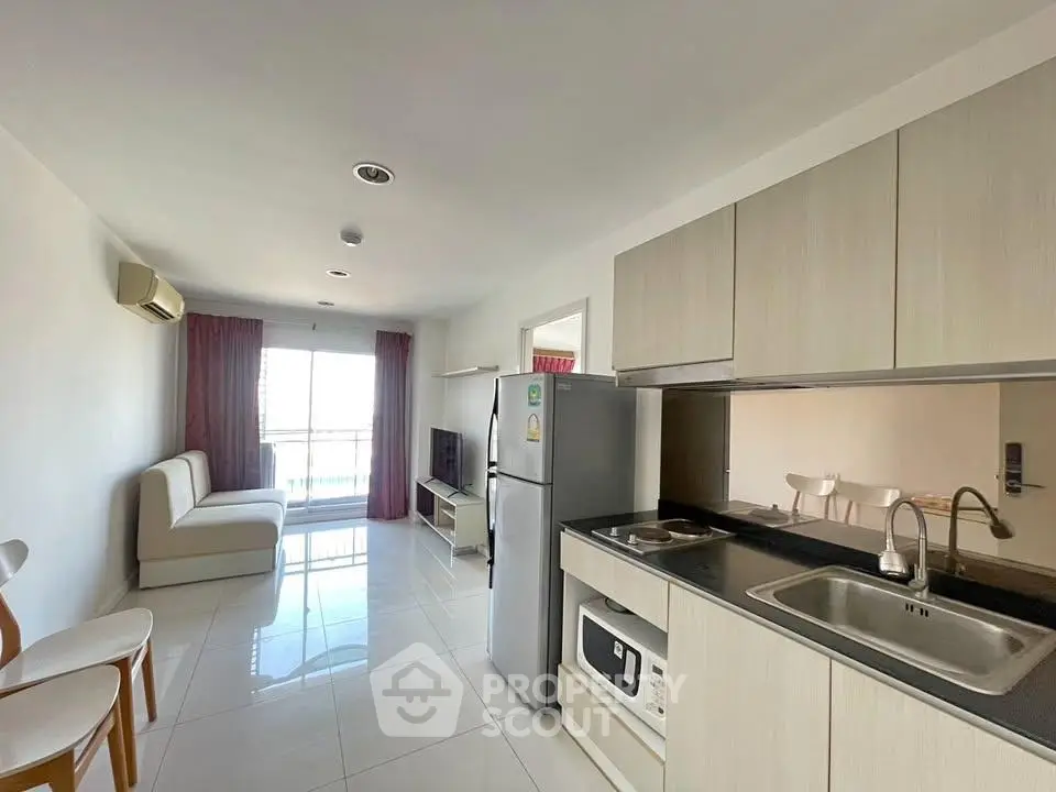 Modern apartment with sleek kitchen and bright living area, featuring a cozy sofa and large window.