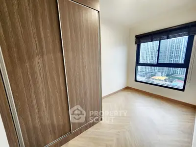 Spacious bedroom with large window and built-in wardrobe offering city views.