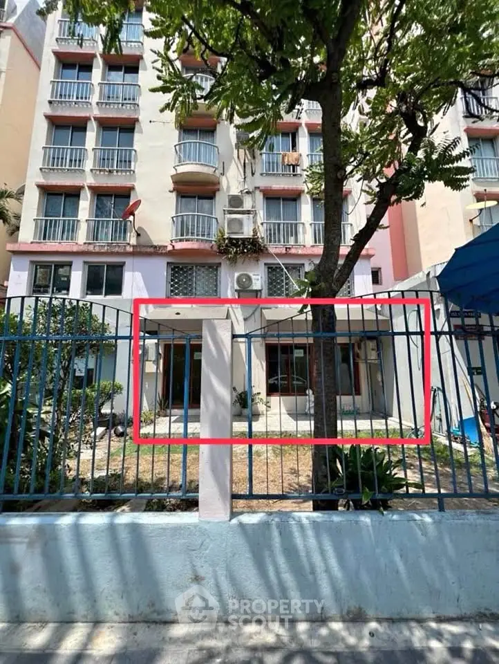 Charming apartment building exterior with lush greenery and secure fencing, ideal for urban living.