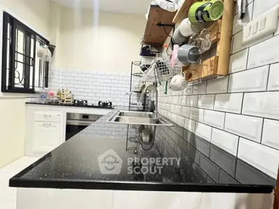 Modern kitchen with sleek black countertop and gas stove, featuring white subway tiles and open shelving.