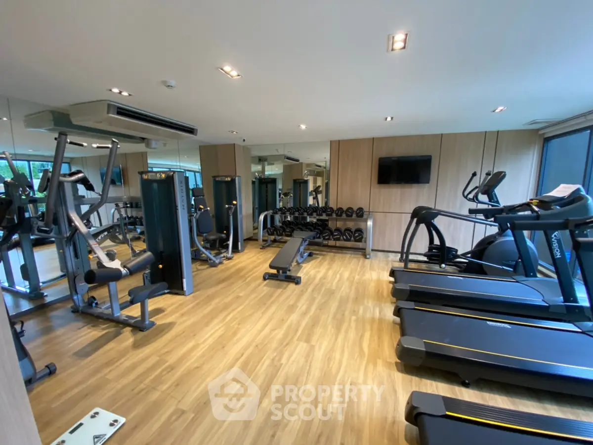 Modern gym with state-of-the-art equipment and wooden flooring in a luxury apartment complex.
