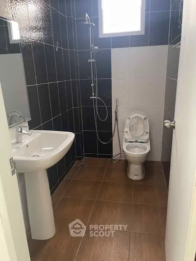 Modern bathroom with sleek black and white tiles, featuring a pedestal sink and shower area.