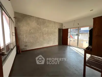 Spacious empty room with large windows and concrete accent wall, perfect for customization.