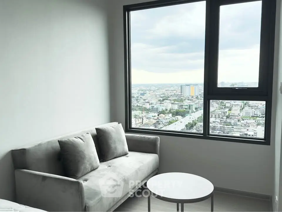 Modern living room with a stunning city view from a large window, featuring a stylish gray sofa and round coffee table.
