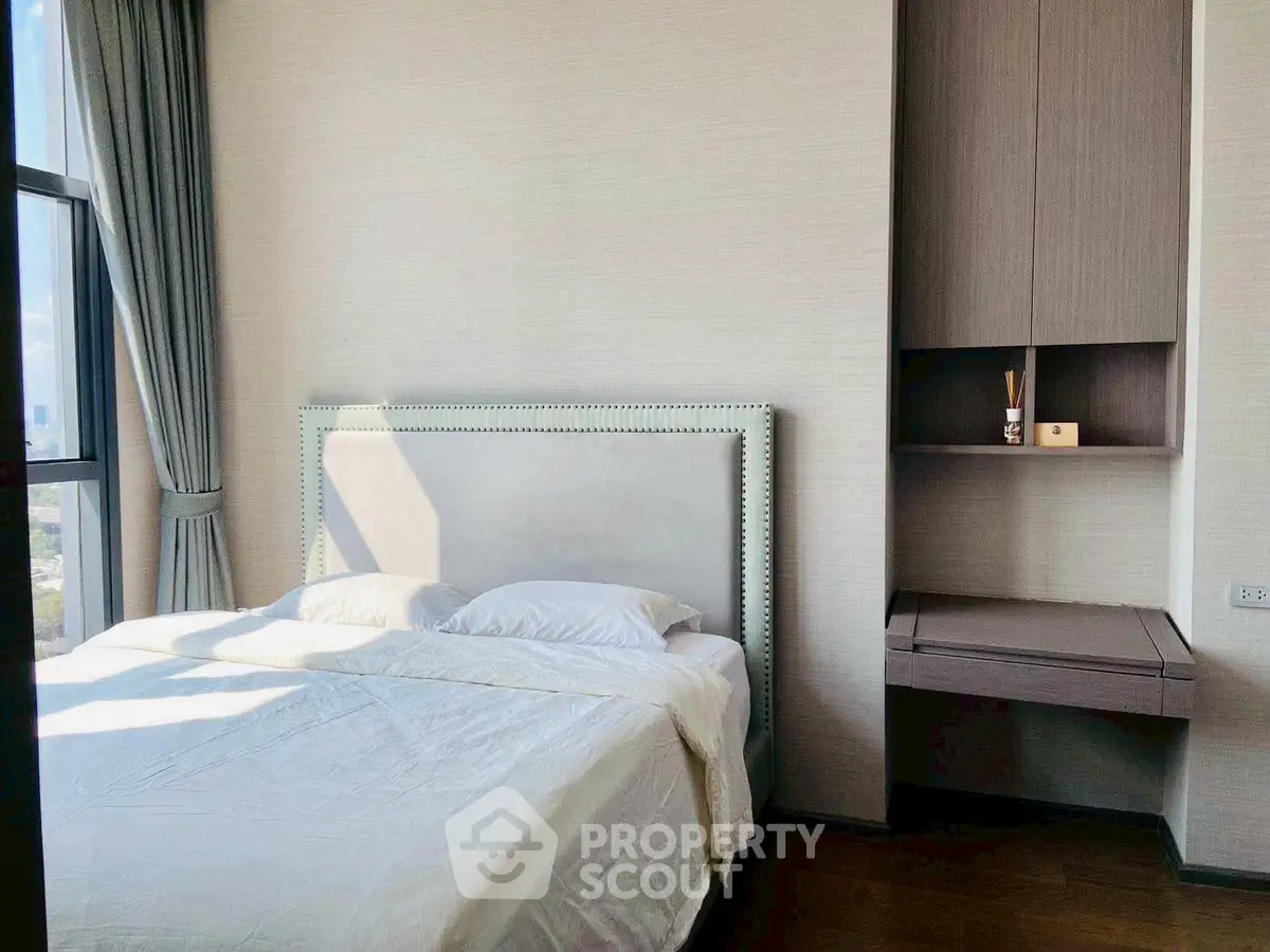 Modern bedroom with elegant bed and built-in storage, featuring large window for natural light.