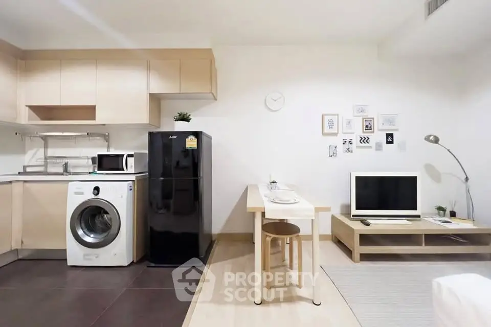 Modern studio apartment with kitchen and living area featuring washing machine and TV setup.